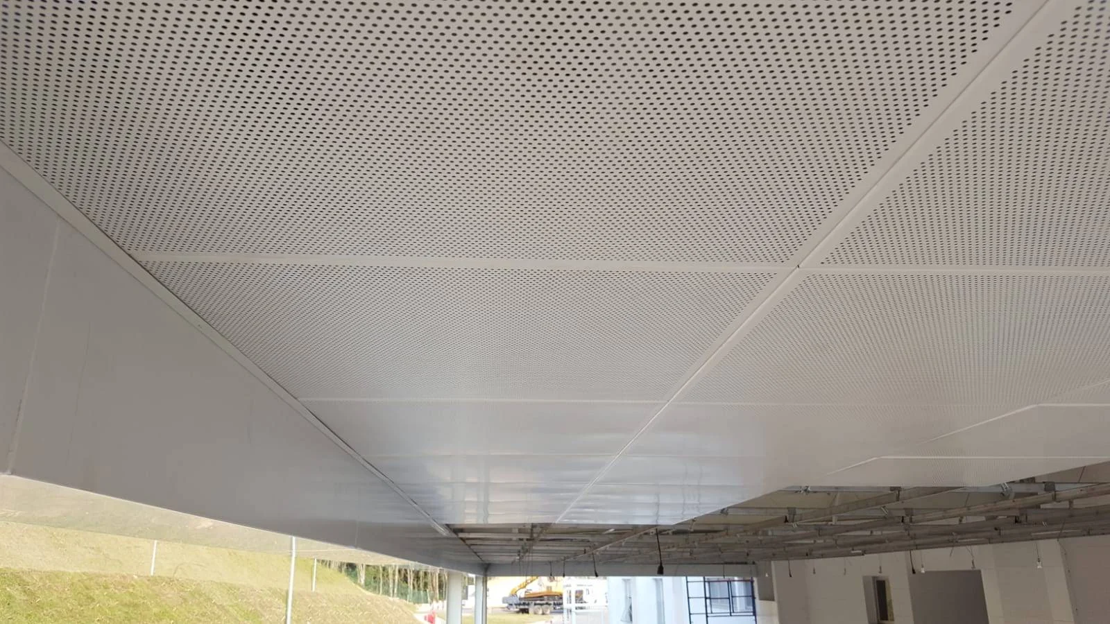 Detalhe de forro com placas perfuradas e parte da estrutura aparente durante a obra.